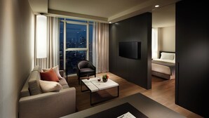 Une chambre d’hôtel moderne équipée d’un canapé, d’un fauteuil, d’une table basse, d’un téléviseur à écran plat et d’un lit.