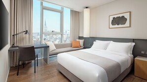 Une chambre d’hôtel moderne, dotée d’un grand lit, d’un bureau, d’une chaise et offrant une vue sur la ville.