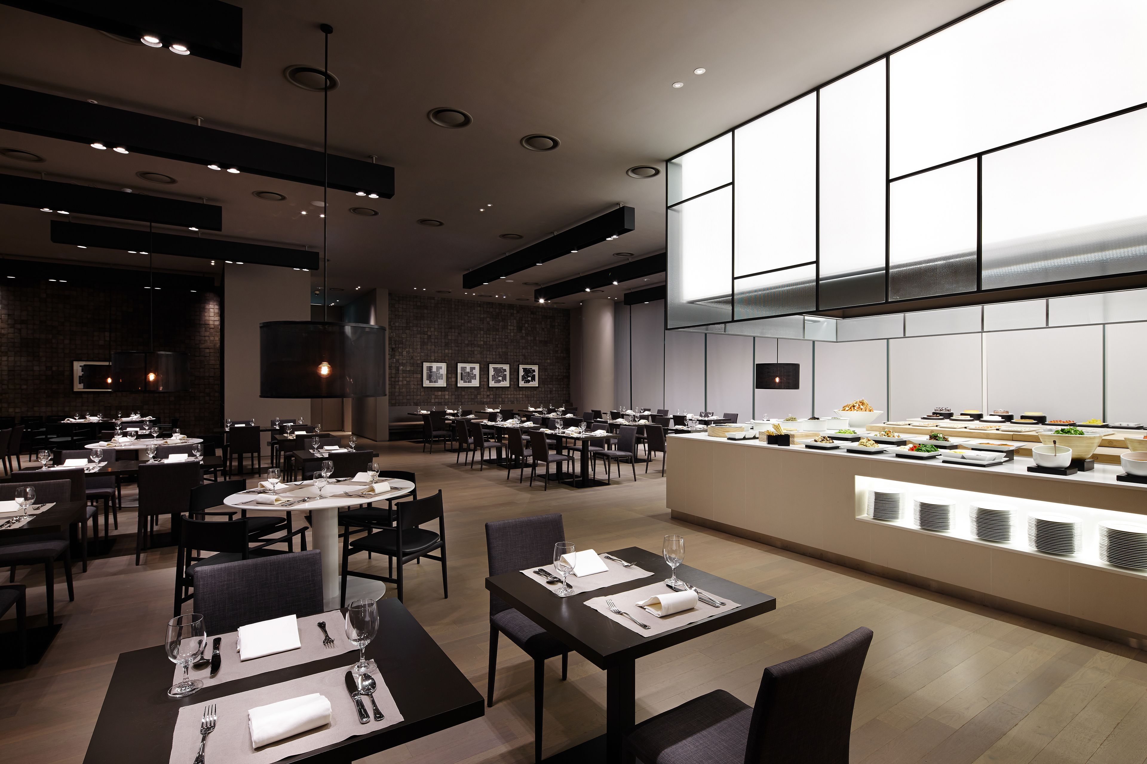 A modern restaurant with multiple dining tables, a central bar area, and a brick wall with framed pictures.