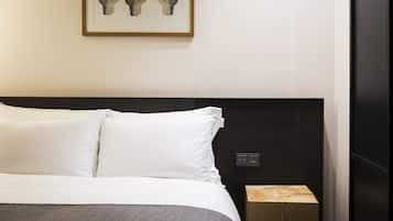 A neatly made bed with white linens, a dark headboard, and a small wooden nightstand beside it.