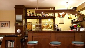A bar area with wooden stools, a shelf with bottles, and glasses. - Pension Schweitzer (Silandro)