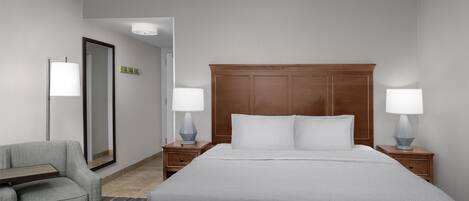 Una camera d'albergo con un letto grande, due comodini con lampade, una sedia e un tavolino.
