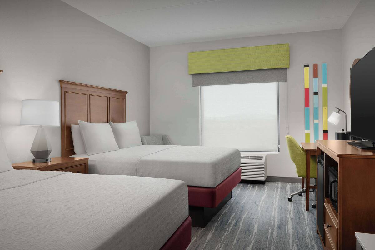 A hotel room with two beds, a desk, a chair, a TV, and a window with a view.