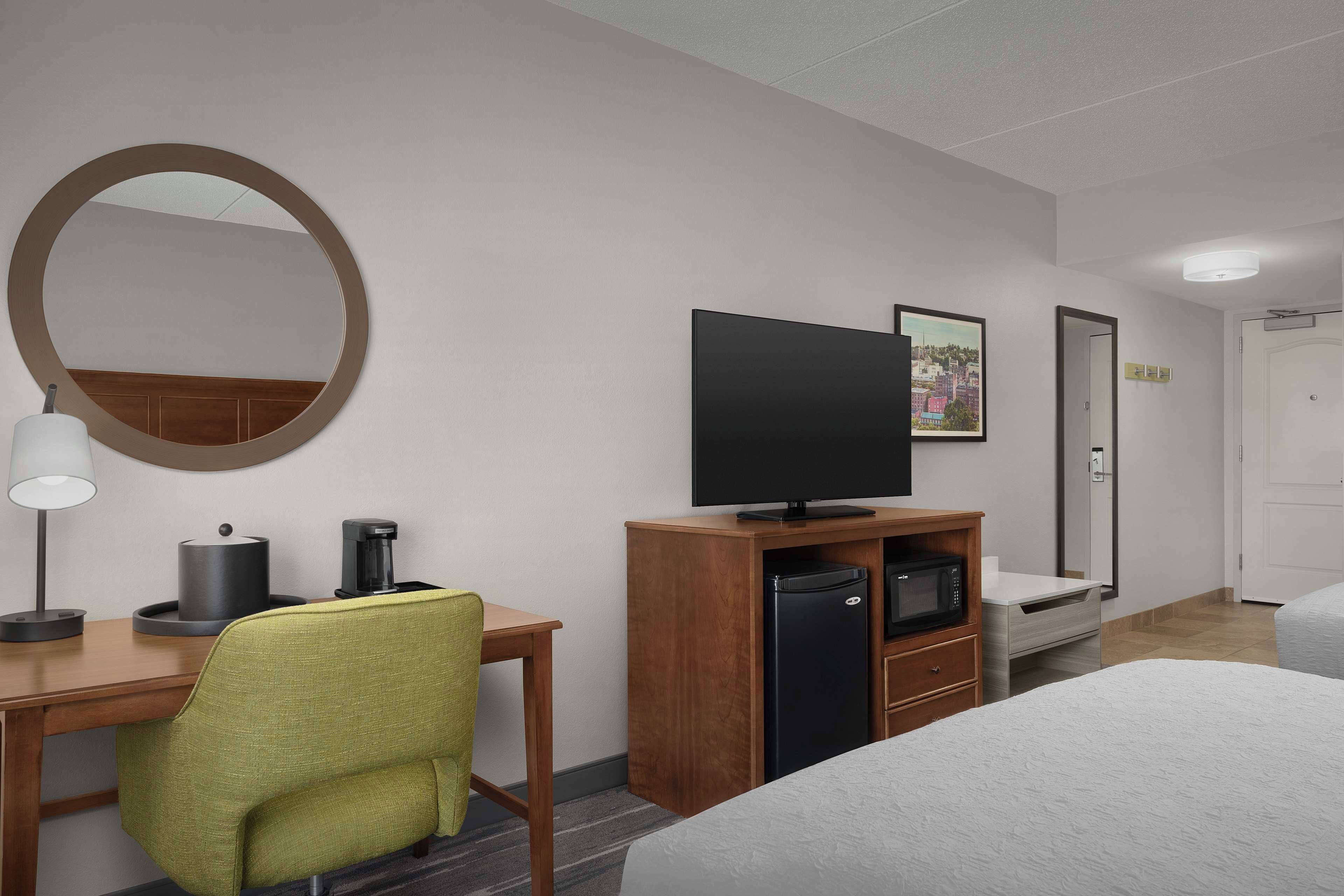 A hotel room with a bed, a desk with a chair, a television, a refrigerator, and a microwave.