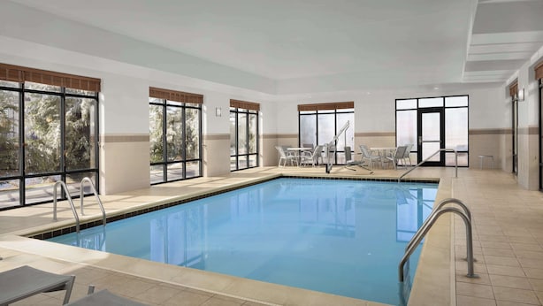 Une piscine intérieure avec des parois en verre transparent, un sol carrelé et plusieurs chaises longues disposées autour de la piscine.