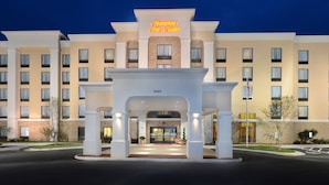 L’entrée d’un hôtel Hampton Inn & Suites, avec une enseigne au néon bien visible, une façade en briques et une adresse numérotée.