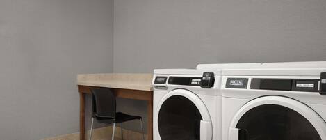 A laundry room with two front-loading washing machines, a wooden table, and a black chair.