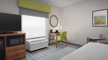 A hotel room with a bed, a desk with a chair, a television, a microwave, and an air conditioning unit.