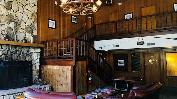 Un interior acogedor con pared de piedra, techo de madera, chimenea, asientos de cuero y una escalera.