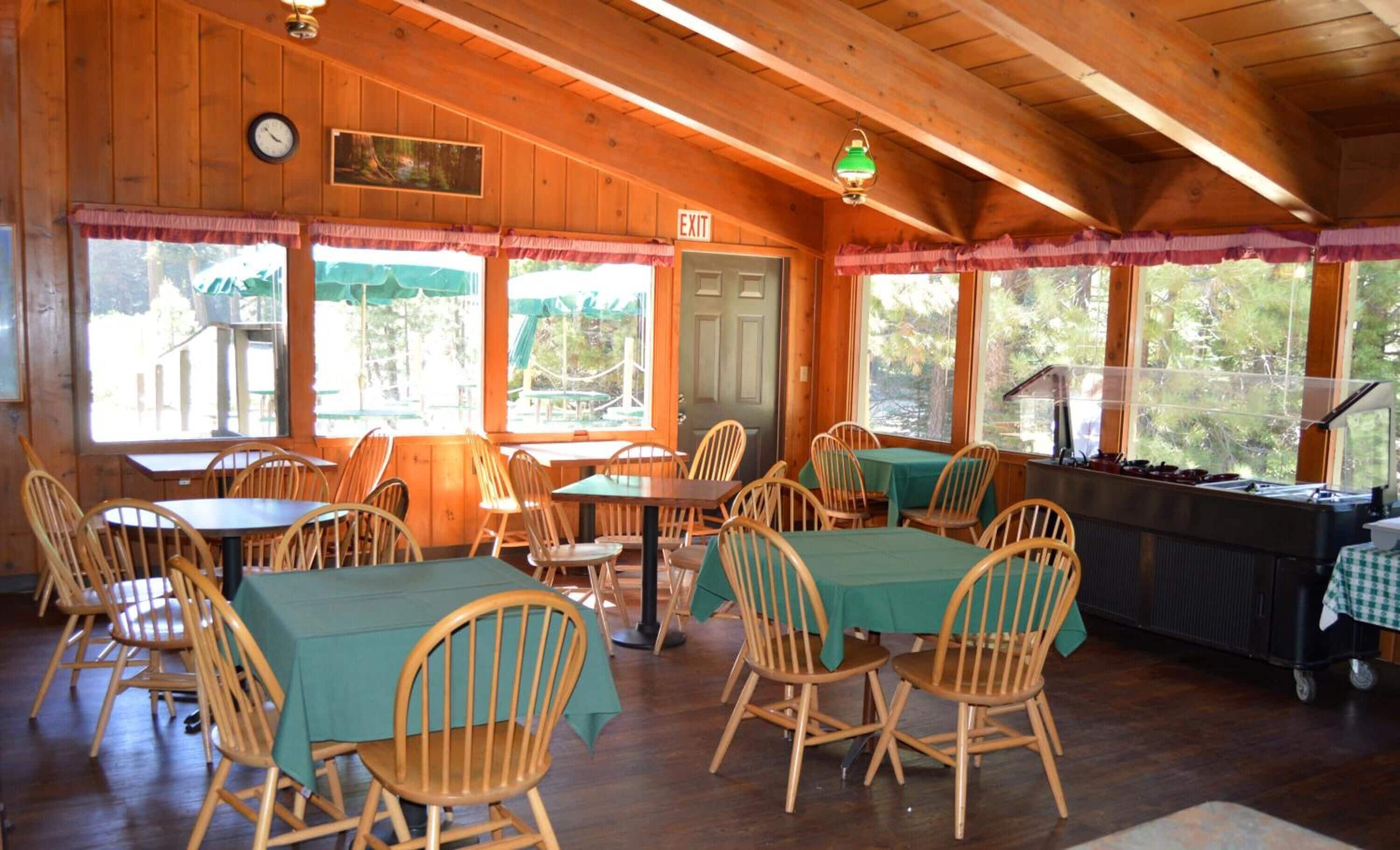 Un comedor acogedor de estilo cabaña, con paredes y techo de madera, manteles verdes y sillas de madera.