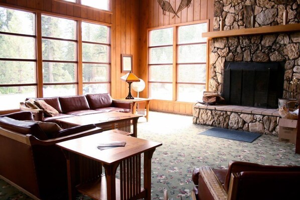 A cozy living room with a stone fireplace, large windows, a sofa, and a coffee table. - Stony Creek Lodge (Kings Canyon National Park)