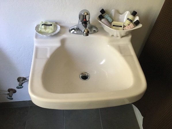 Un lavabo blanc amb aixeta cromada, plat per al sabó i suport per a diversos productes de tocador.