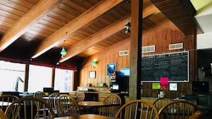 Un interior rústico de madera con mesas y sillas, un menú en una pizarra y un televisor.