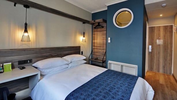 Habitació d'hotel amb un llit, una taula de nit i un mirall a la paret.