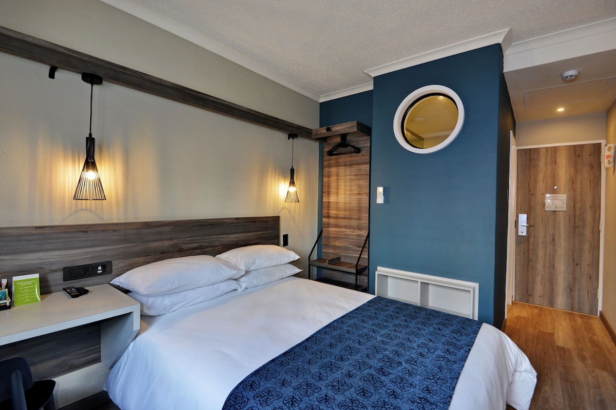 A hotel room with a bed, bedside table, and a mirror on the wall.