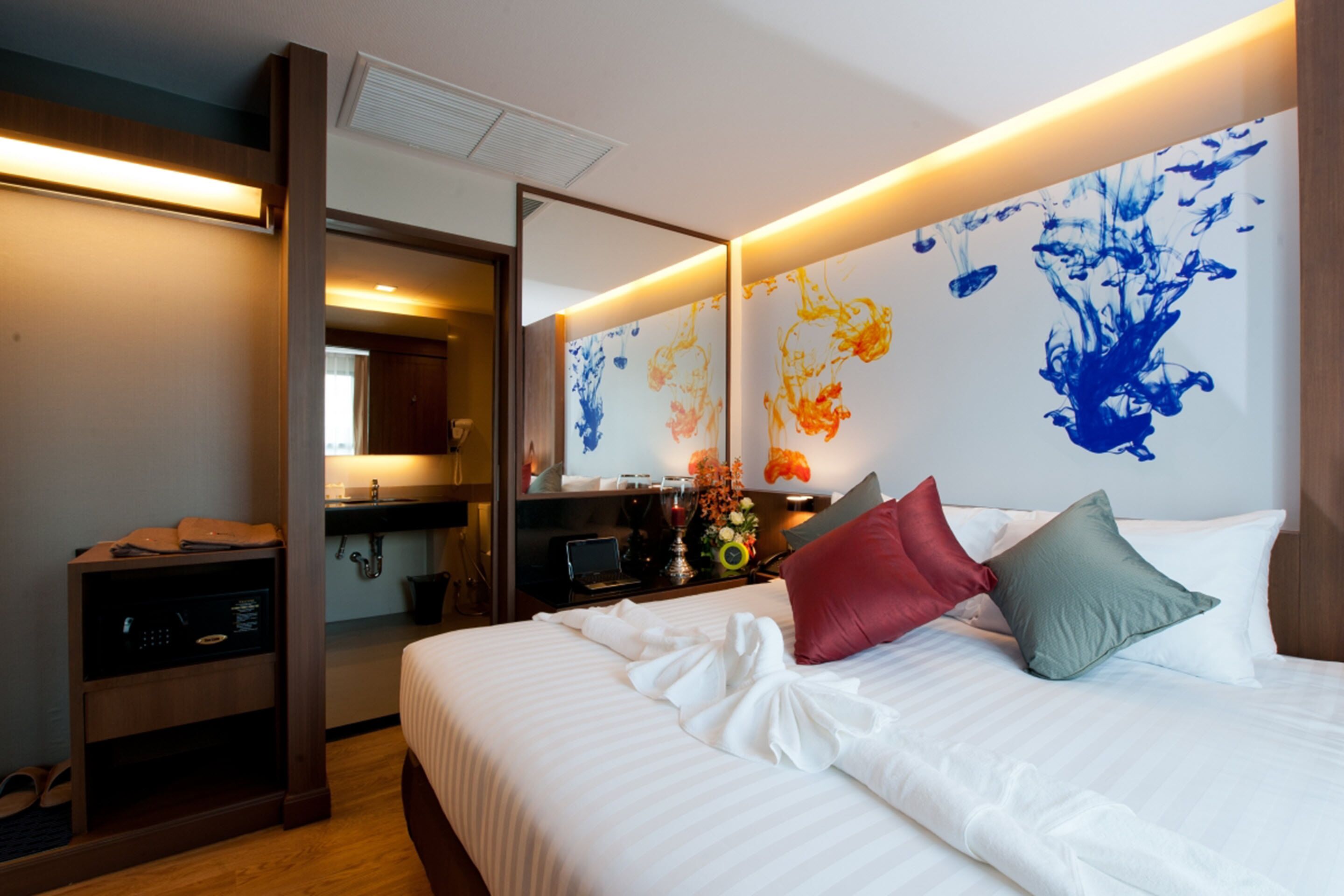 Une chambre d’hôtel avec un lit soigneusement fait, un bureau avec un ordinateur et une salle de bain visible à travers une porte ouverte.