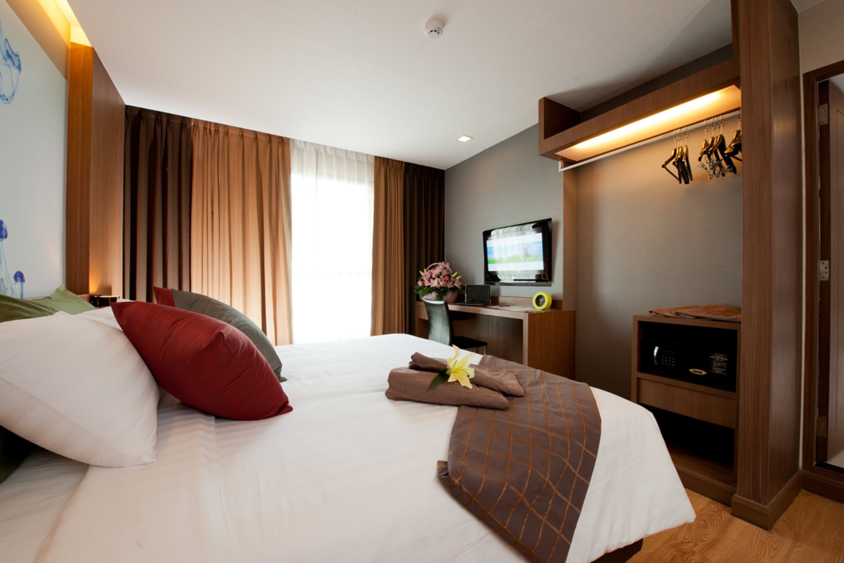 A hotel room with a bed, a desk with a computer, a television, and a small shelf with items.