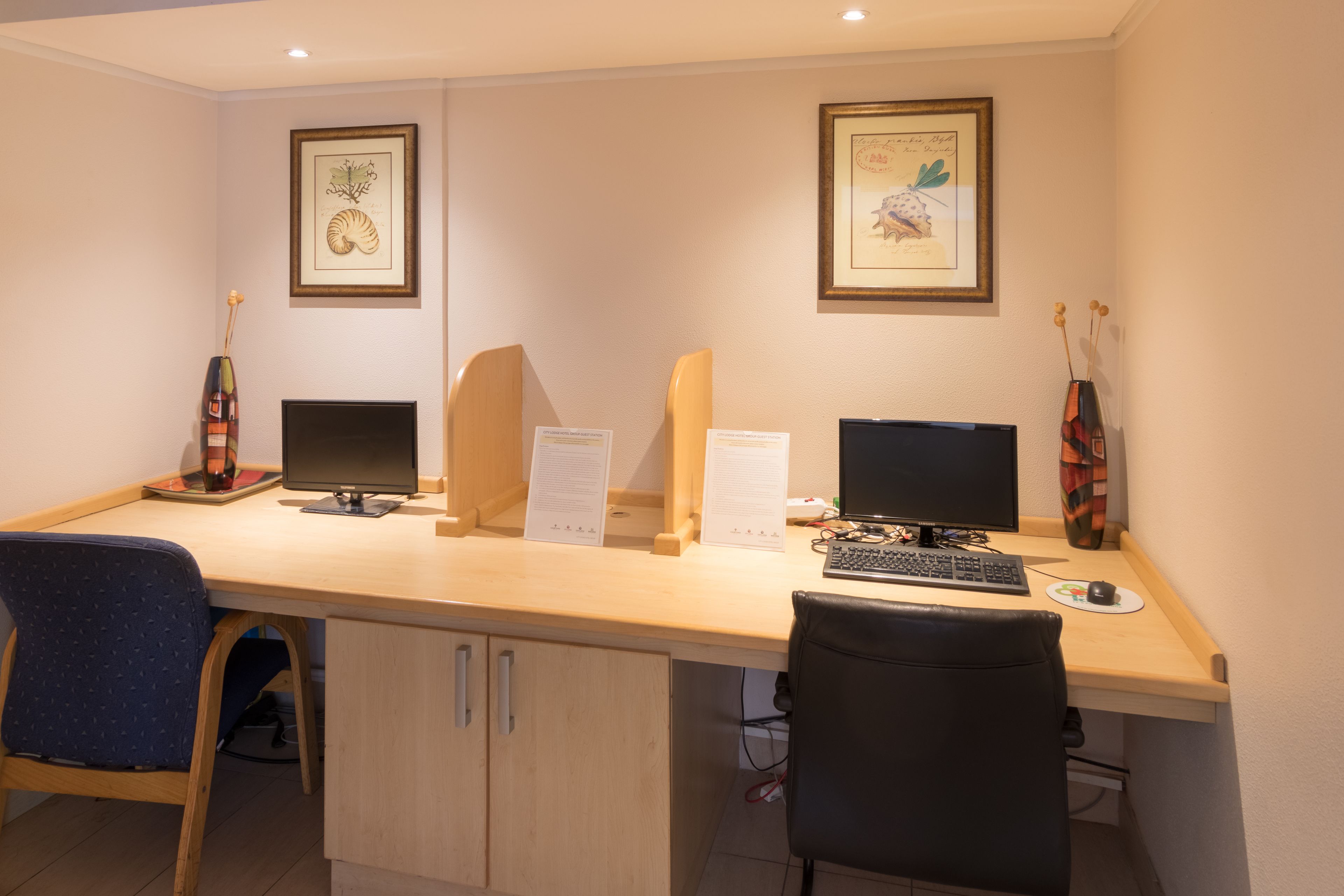 Habitación de hotel con un escritorio de madera, dos monitores de computadora, un teclado, un ratón y dos sillas.