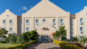 Um hotel com vários andares, entrada central e área verde circundante, com calçada pavimentada.