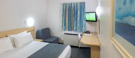 A hotel room with a bed, a desk, a chair, a television, and a window with curtains.