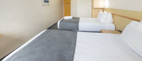 A hotel room with two beds, a wooden headboard, a painting on the wall, and a door in the background.