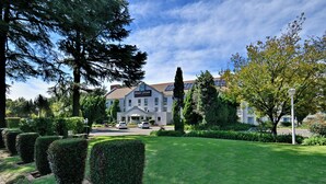 Um hotel com gramado bem cuidado, sebes bem aparadas e vista clara para a entrada do edifício.