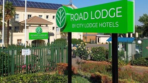 Letrero de Road Lodge by City Lodge Hotels con logotipo verde, entrada con portón y un edificio con paneles solares al fondo.