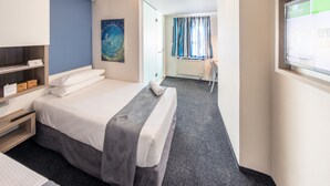 Una habitación de hotel con una cama, una mesita de noche y un escritorio con una silla.