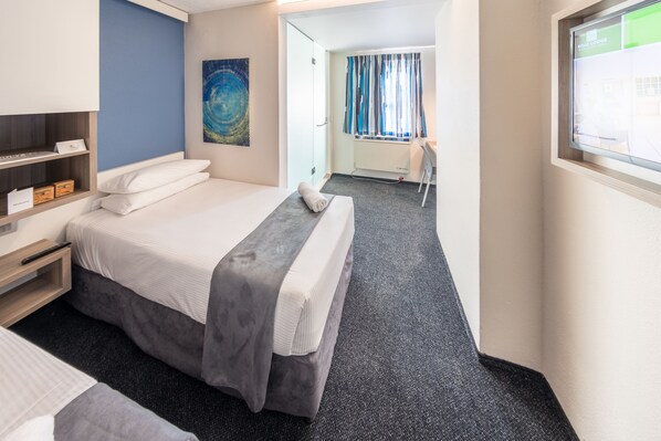 A hotel room with a bed, bedside table, and a desk with a chair.