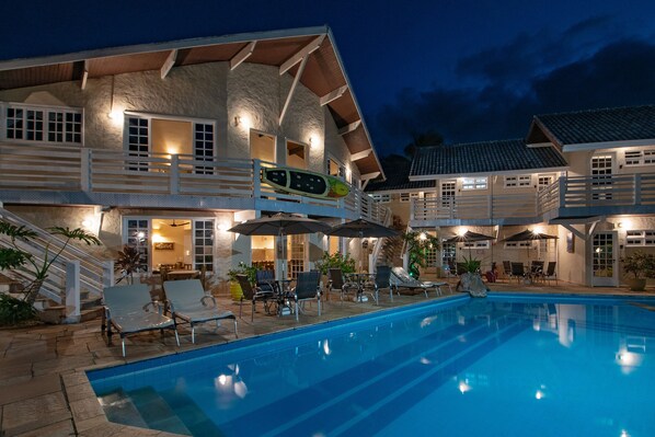 Una casa grande con piscina, mobiliario exterior y una zona cubierta con sombrillas.