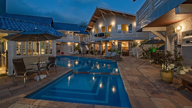 A pool area with lounge chairs, a covered seating area, and a staircase leading to a second floor. - Pauba Beach Hotel (São Sebastião)