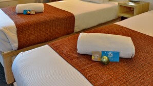 Two hotel beds with white linens and brown blankets, a small card on one bed, and a nightstand with a lamp.
