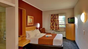 Ein Hotelzimmer mit Bett, Schreibtisch, Sessel, Fernseher und einem Vorhangfenster.