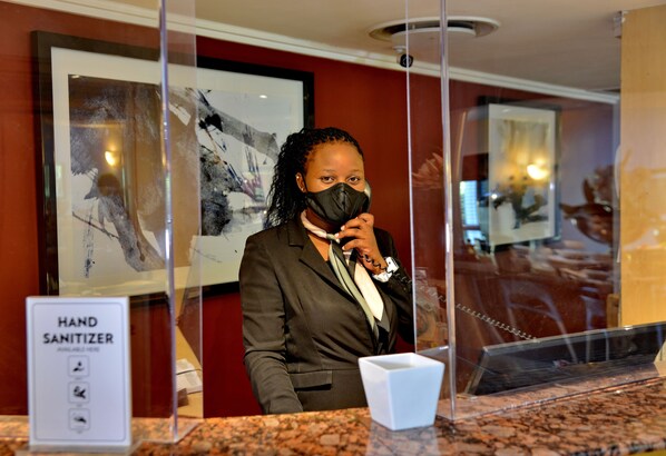A hotel reception area with a hand sanitizer dispenser, framed artwork on the wall, and a marble counter.