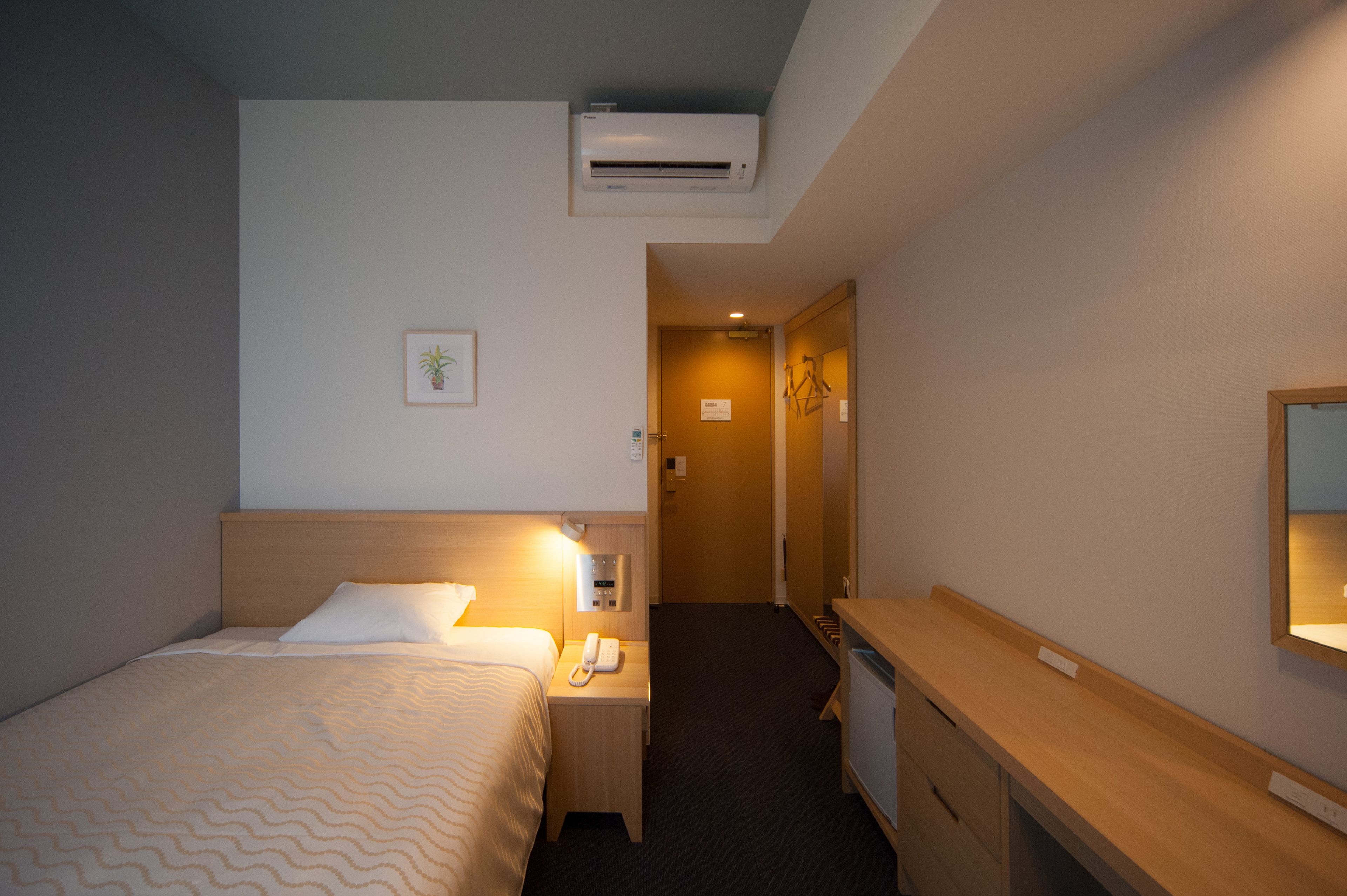 Habitación de hotel con cama, mesita de noche, lámpara, aire acondicionado y escritorio con espejo.