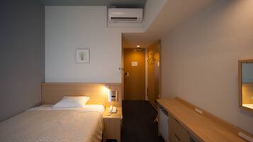 Habitación de hotel con cama, mesita de noche, lámpara, aire acondicionado y escritorio con espejo.