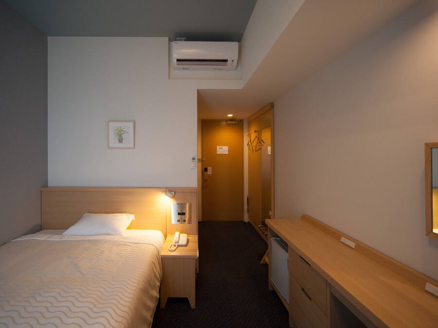 Habitación de hotel con cama, mesita de noche, lámpara, aire acondicionado y escritorio con espejo.
