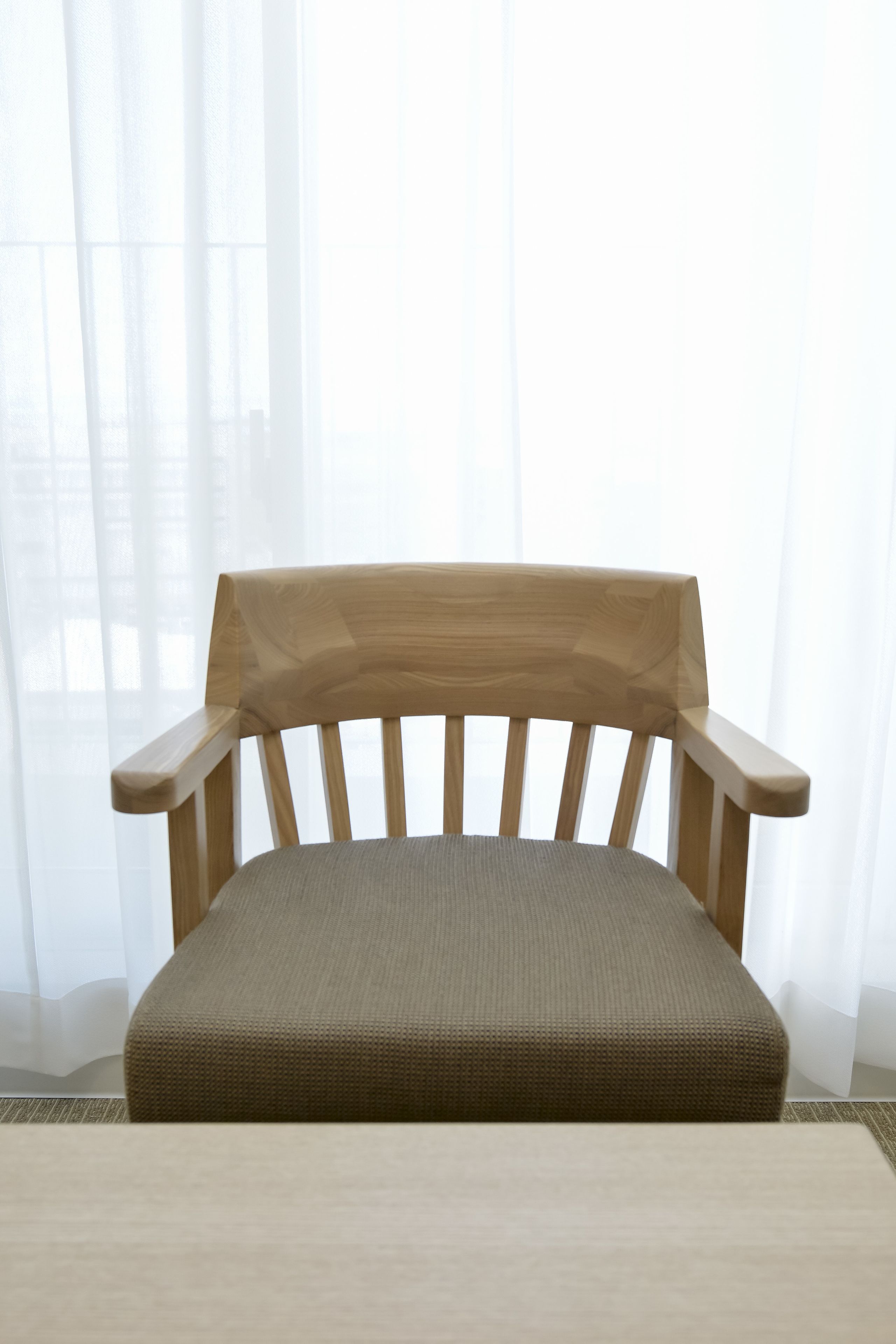 Un banco de madera con asiento y respaldo acolchados, ubicado frente a cortinas blancas traslúcidas.