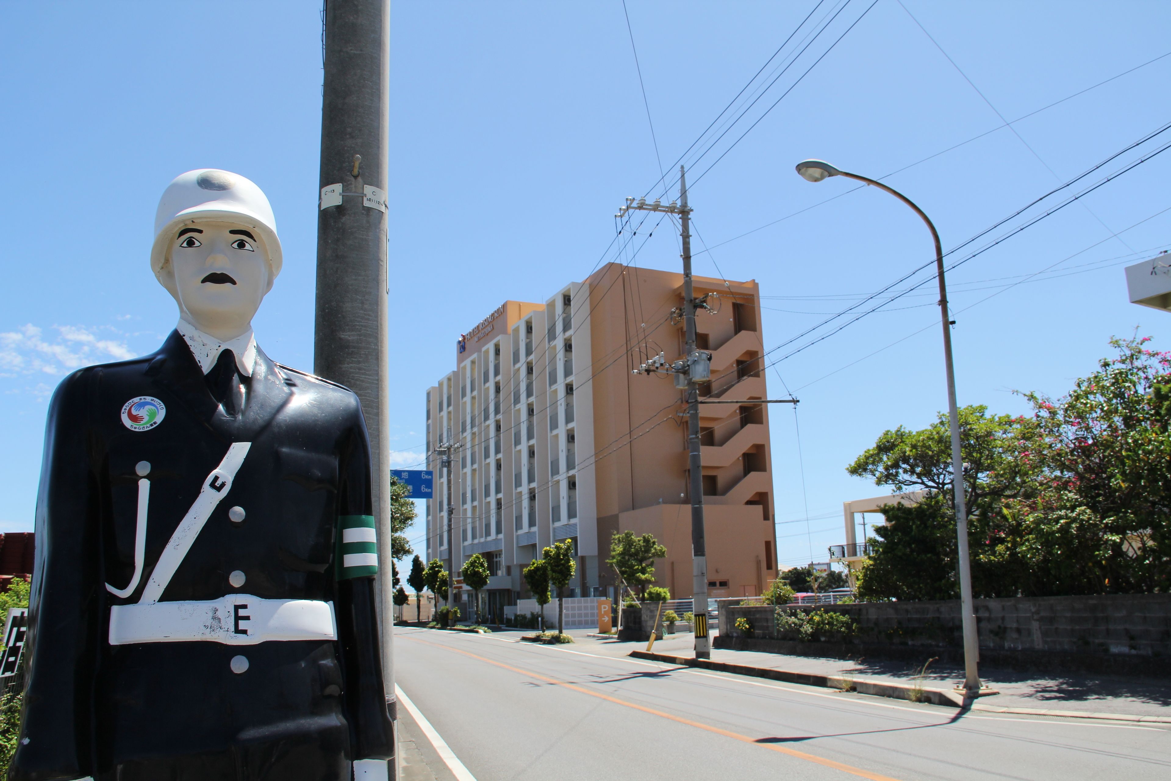 A statue of a man in uniform on a street with a multi-story building in the background.
