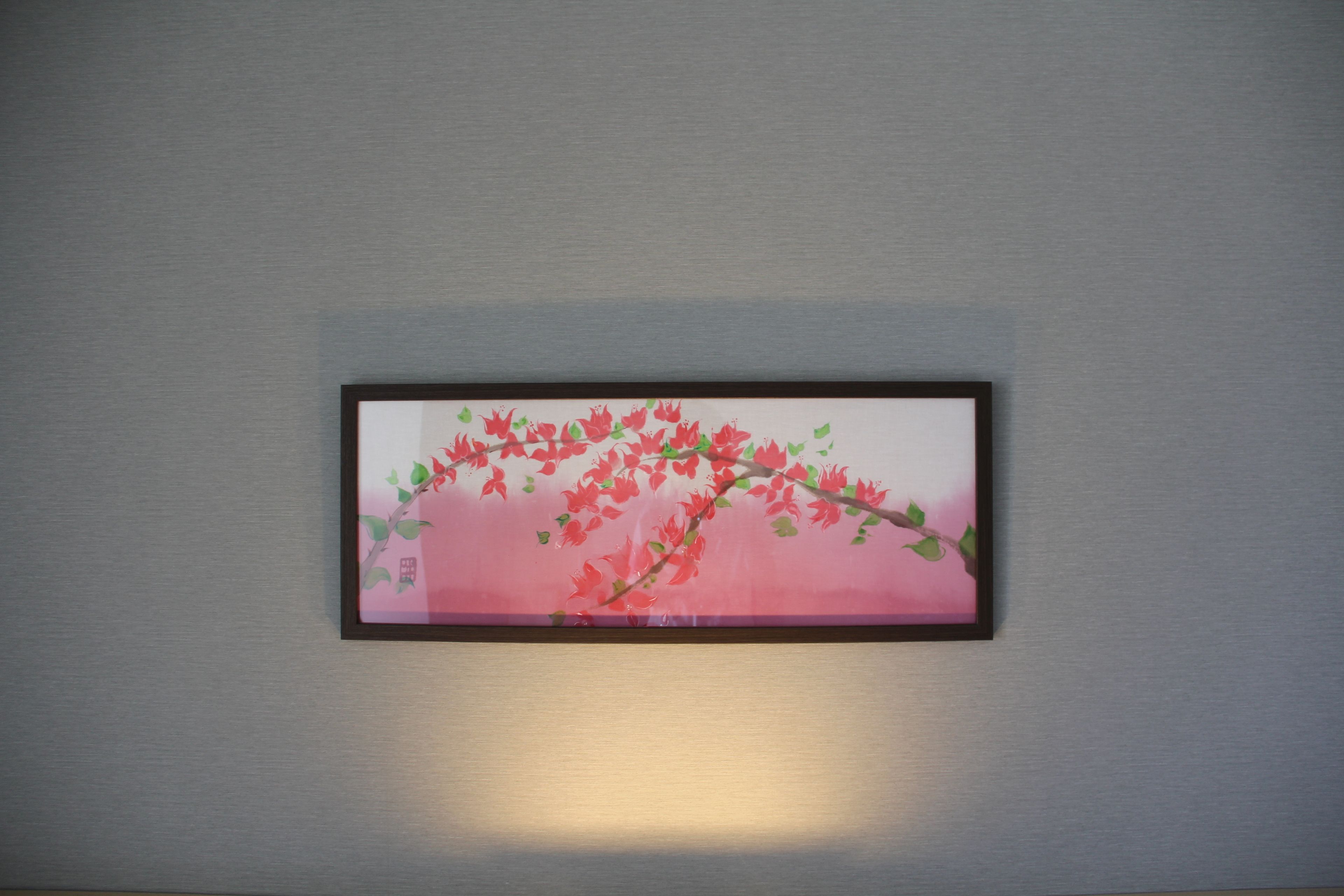 A framed artwork of a red and green branch on a grey wall.