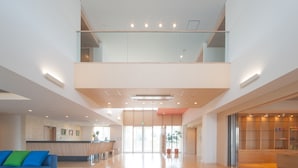 A spacious lobby with a reception desk, a blue sofa, and a staircase leading to an upper level. - Hotel Rising Sun Miyakojima (Miyakojima)