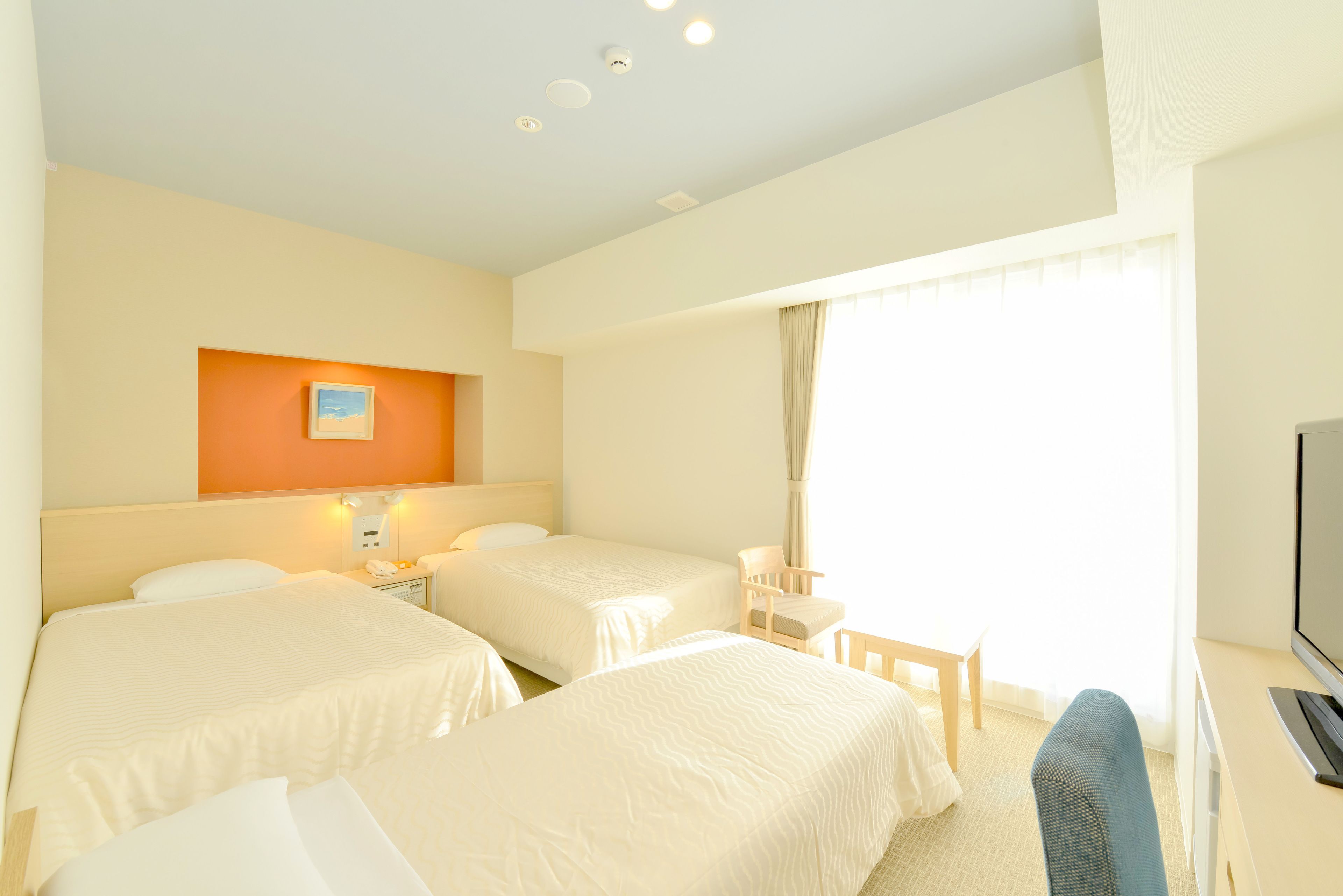 Habitación de hotel con dos camas, un escritorio, una silla, un televisor y una ventana con cortinas.