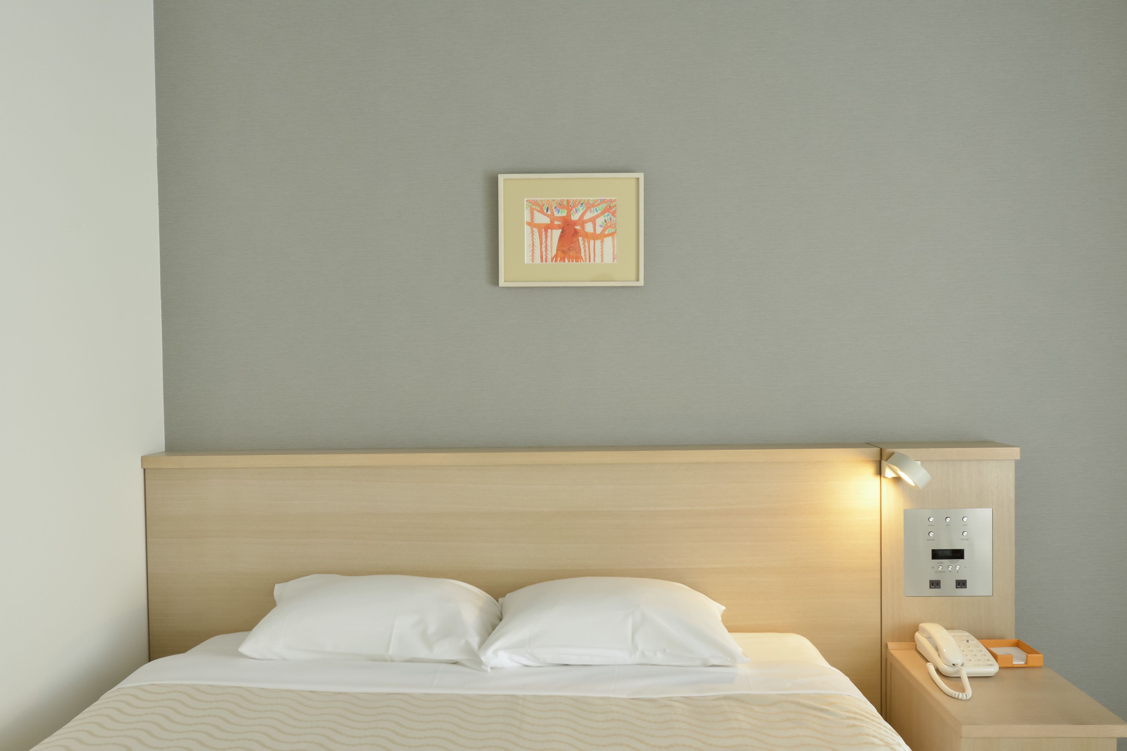 A neatly made bed with white linens, a bedside table with a white telephone, and a wall-mounted light.