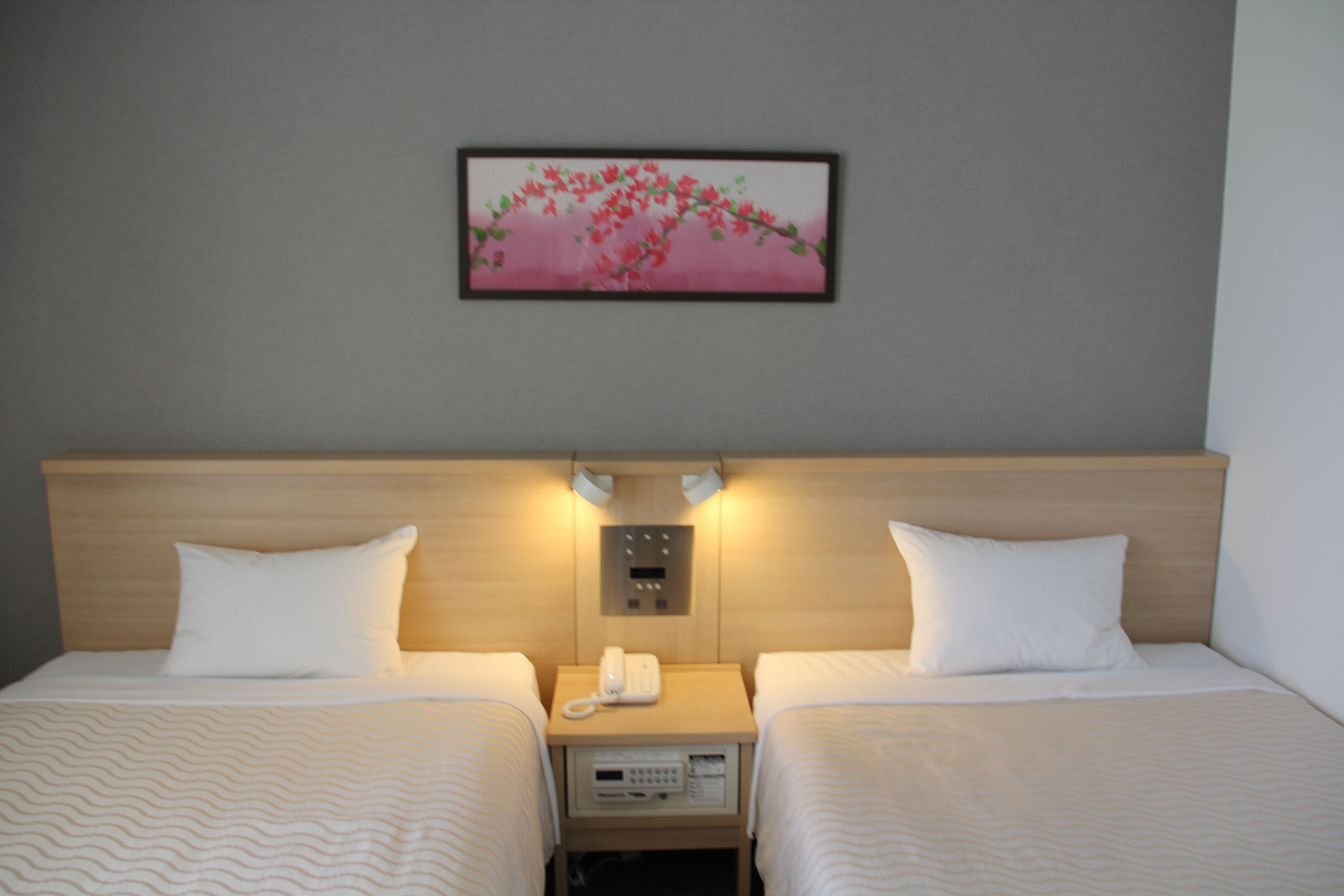 A hotel room with two beds, a bedside table with a phone, and a wall-mounted artwork.