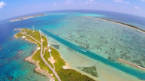 An aerial view of a coastal area with wind turbines, a road, and clear blue waters. - Hotel Rising Sun Miyakojima (Miyakojima)