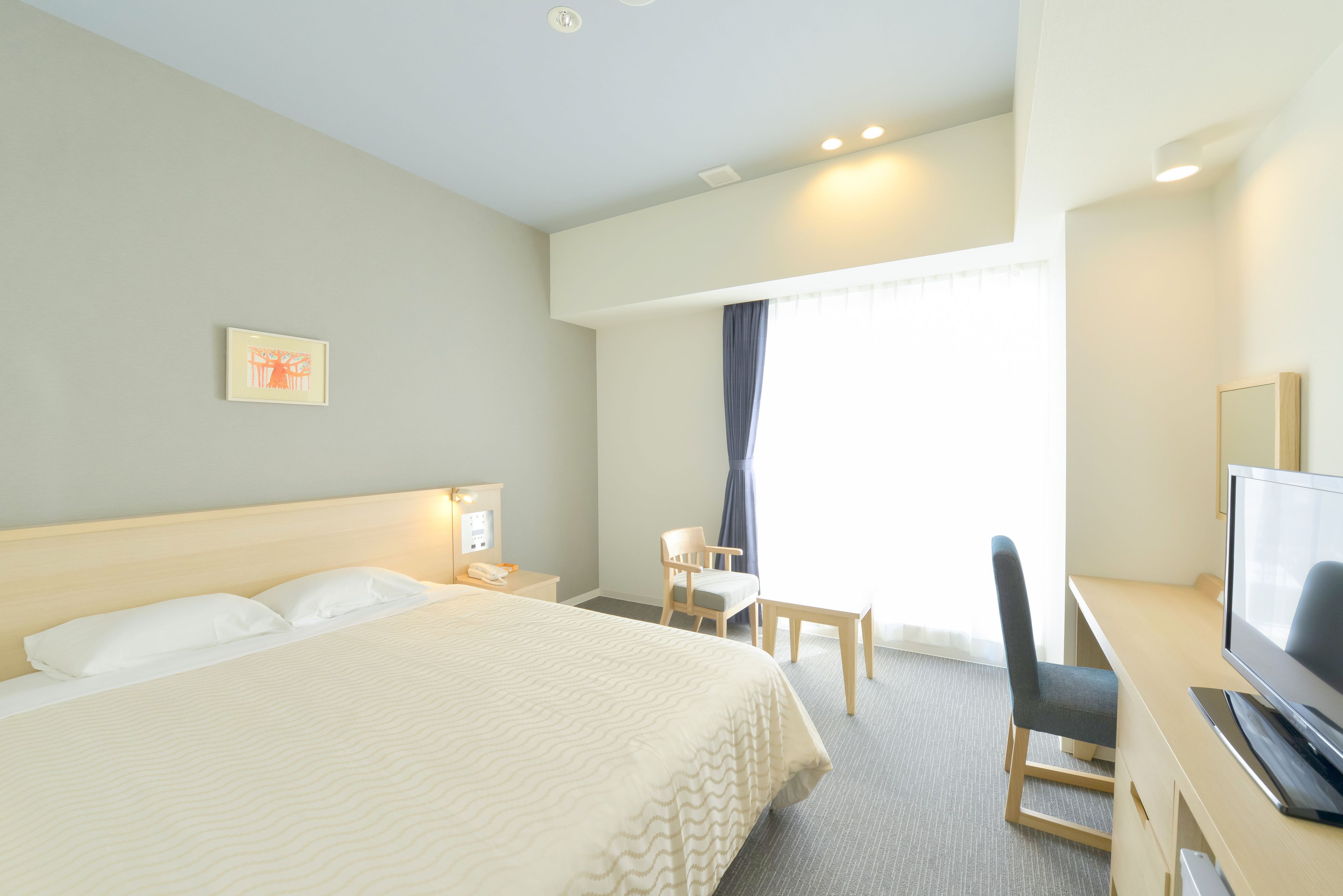 Una habitación de hotel con una cama, un escritorio con televisor, una silla y una ventana con cortinas.