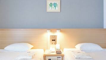 A hotel room with two beds, a bedside table with a phone and a lamp, and a wall-mounted control panel.