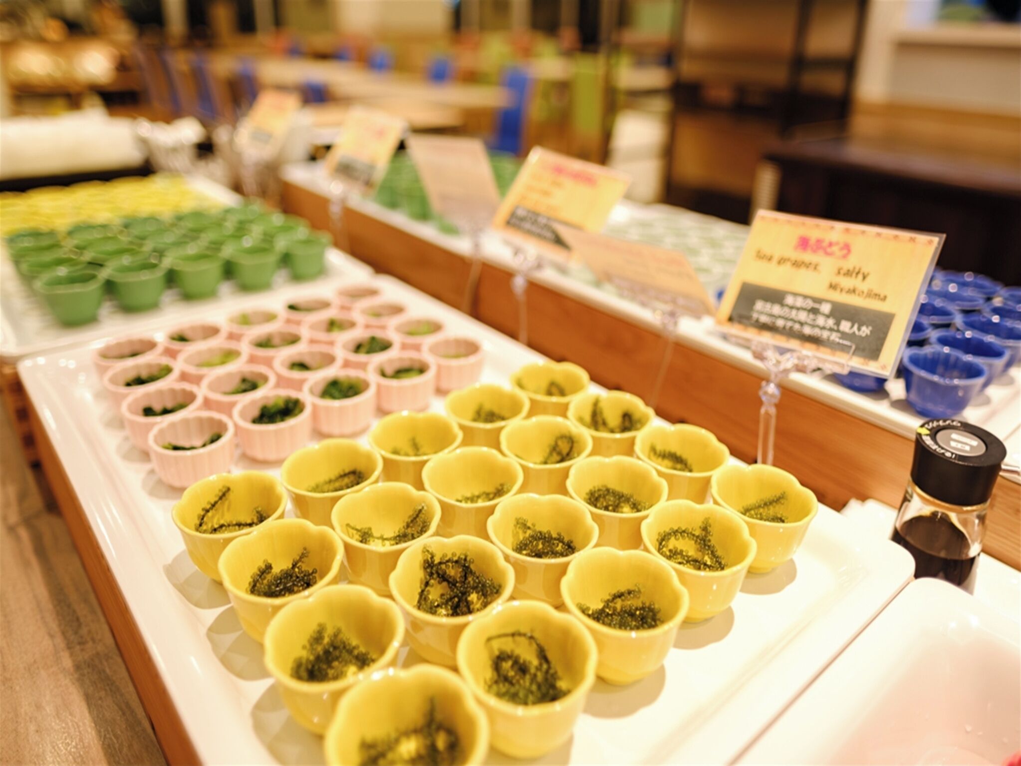 A display of various colored cups filled with green tea leaves, arranged on a white tray.