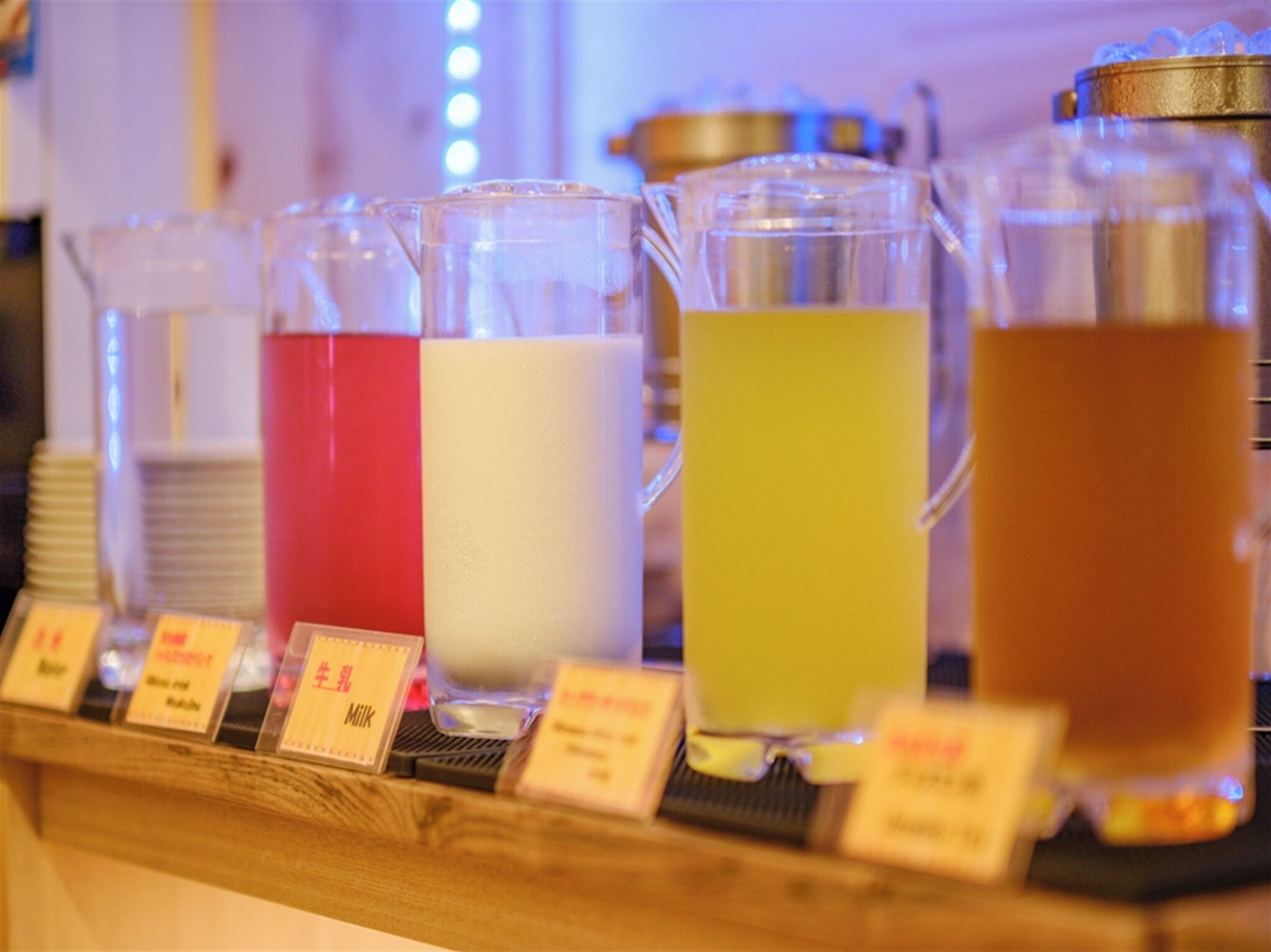 A beverage station with various drinks in pitchers, each labeled with a different name.