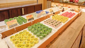 A food display with various dishes in colorful cups, a counter with a cash register, and a person in the background. - Hotel Rising Sun Miyakojima (Miyakojima)